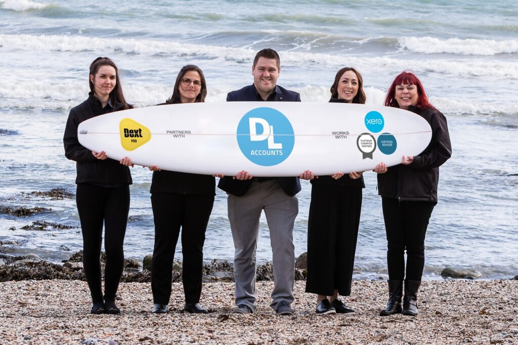 The accountancy team holding a surfboard displaying logos of digital accounting software they use, Dext and Xero.